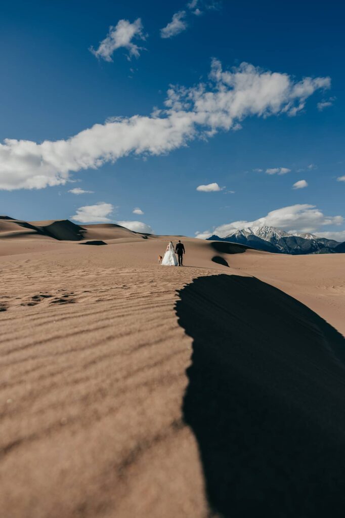 a couple during their great sand dunes elopement walking away with their dog